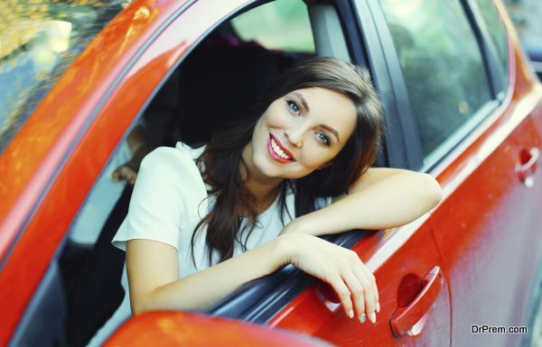 Beautiful smiling woman driver behind the wheel red car