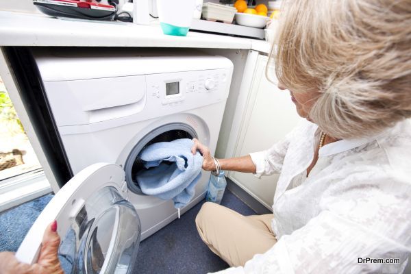 Senior woman loading towel in washing machine at home