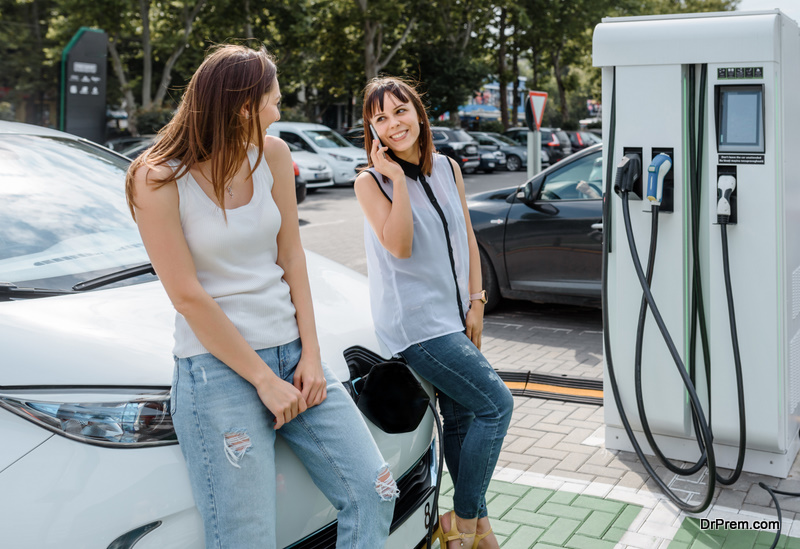 Two happy young beautiful women are talking to each other until their electric car is charging at the charging station