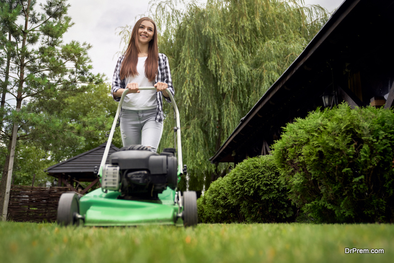 Front below view of pretty young smiling woman using lawn mower on backyard.