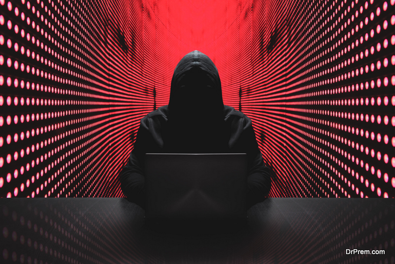 Anonymous hacker in front of his computer with red light wall background