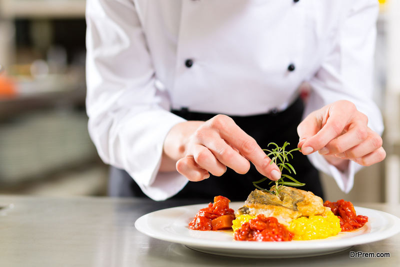 Female Chef in hotel or restaurant kitchen cooking, only hands, she is finishing a dish on plate