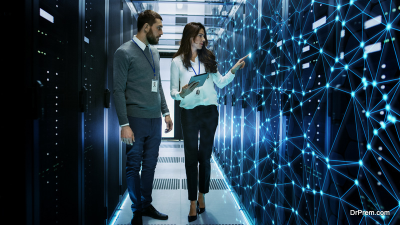 Female and Male IT Engineers Discussing Technical Details in a Working Data Center Server Room.