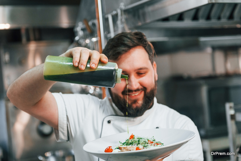 Pouring oil on the salad. Professional chef preparing food in the kitchen.