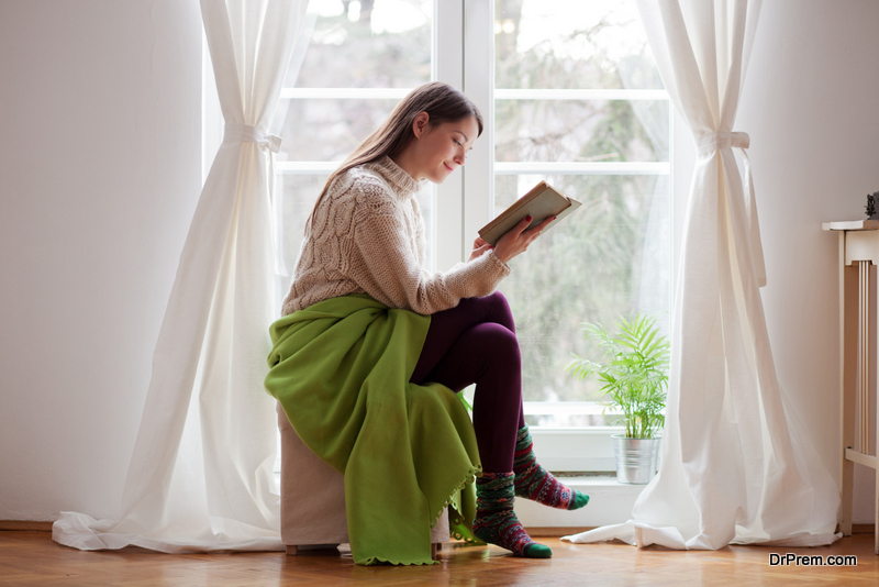Beautiful young woman sitting by the window reading a book