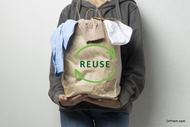 Woman holding paper bag full of clothes against white empty wall